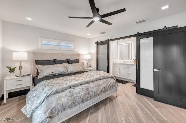 bedroom with a barn door, visible vents, a ceiling fan, light wood-style flooring, and ensuite bathroom