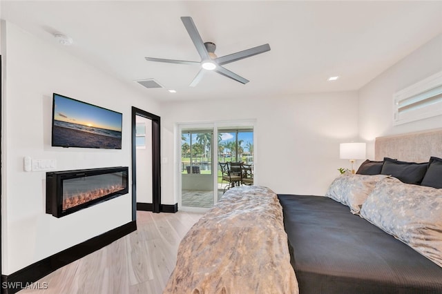 bedroom with visible vents, baseboards, access to outside, light wood-type flooring, and a glass covered fireplace