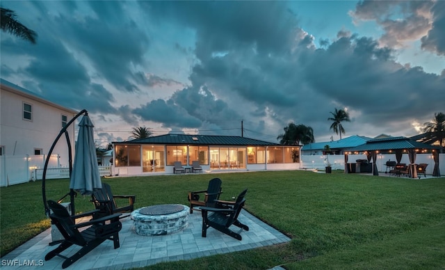 back of property featuring metal roof, a fire pit, a gazebo, a lawn, and a patio area