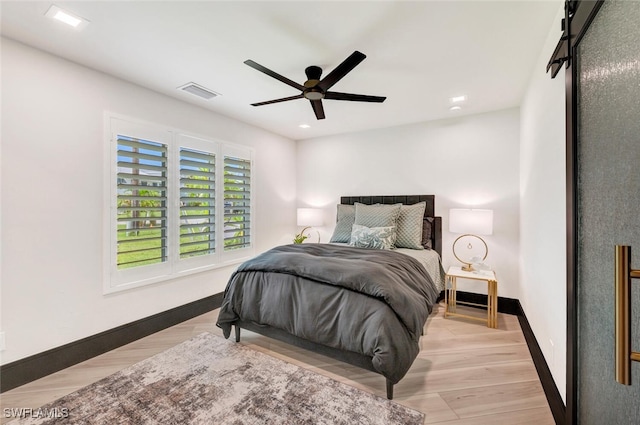 bedroom with a barn door, ceiling fan, and light hardwood / wood-style floors