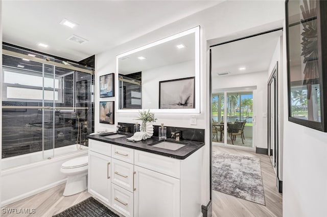 bathroom featuring toilet, shower / bath combination with glass door, wood finished floors, a sink, and double vanity