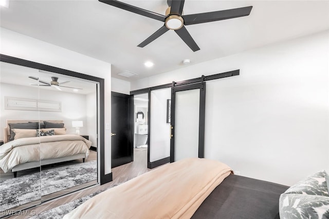 bedroom with ceiling fan, a barn door, recessed lighting, wood finished floors, and a closet