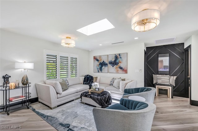 living area with a skylight, baseboards, visible vents, and light wood finished floors