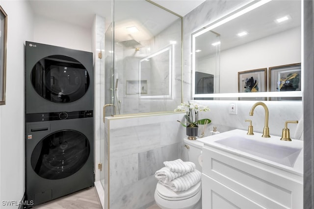 bathroom featuring tile walls, toilet, stacked washer / drying machine, and vanity