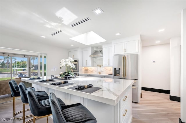 kitchen featuring light hardwood / wood-style floors, light stone countertops, a skylight, white cabinets, and wall chimney exhaust hood