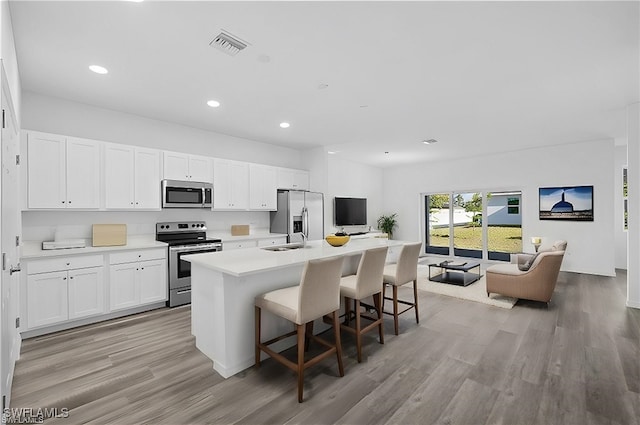 kitchen featuring stainless steel appliances, a center island with sink, white cabinets, light hardwood / wood-style floors, and a breakfast bar area