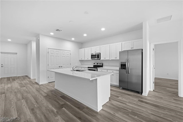 kitchen with sink, stainless steel appliances, an island with sink, white cabinets, and hardwood / wood-style flooring