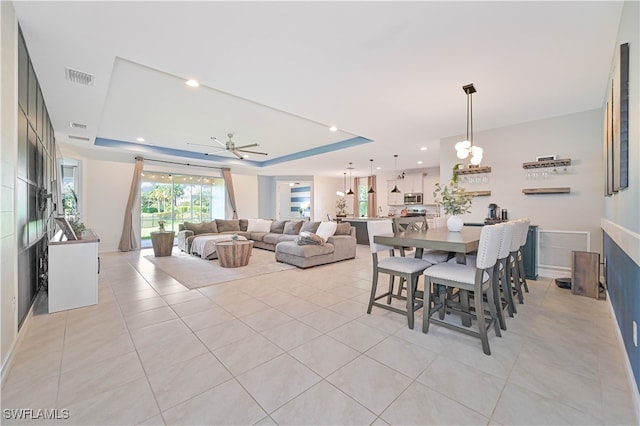 dining area featuring a raised ceiling, ceiling fan with notable chandelier, and light tile patterned flooring