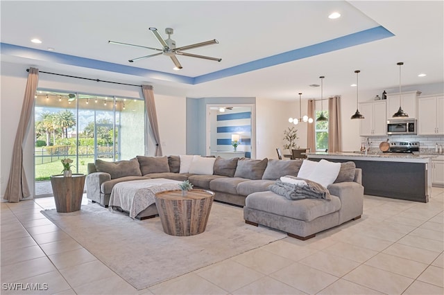 living room featuring a tray ceiling, ceiling fan with notable chandelier, and light tile patterned floors