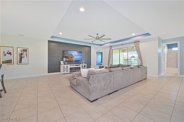 living room featuring ceiling fan, a raised ceiling, and light tile patterned floors