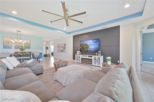 tiled living room with a tray ceiling, tile walls, and ceiling fan with notable chandelier