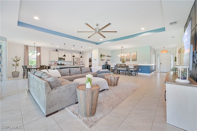 living room featuring a tray ceiling, light tile patterned flooring, and ceiling fan with notable chandelier