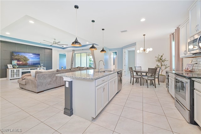 kitchen with sink, light stone countertops, ceiling fan with notable chandelier, stainless steel appliances, and white cabinets