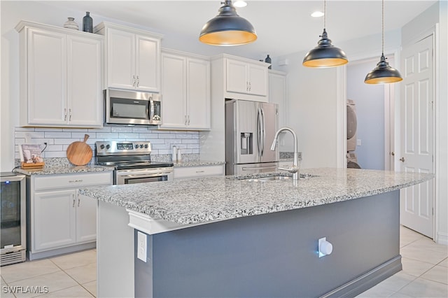 kitchen with appliances with stainless steel finishes, an island with sink, light tile patterned floors, and backsplash