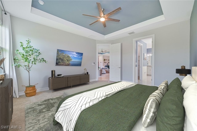 bedroom with ceiling fan, a raised ceiling, light colored carpet, and ensuite bathroom