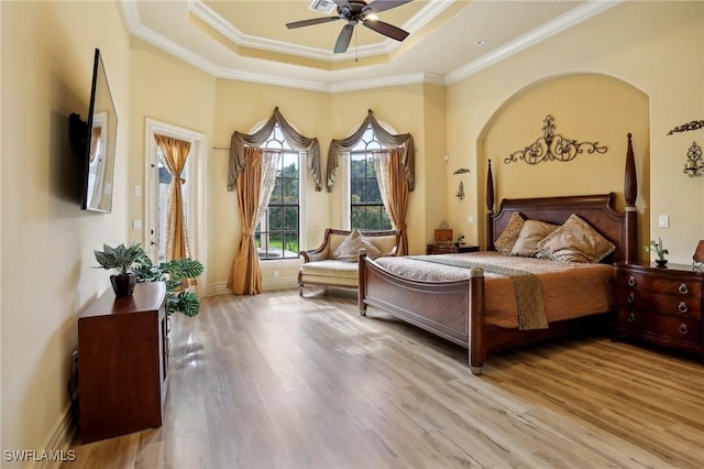 bedroom with crown molding, a tray ceiling, and light wood-type flooring