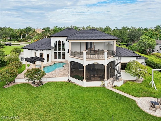 rear view of property featuring a balcony, a sunroom, a patio area, and a lawn