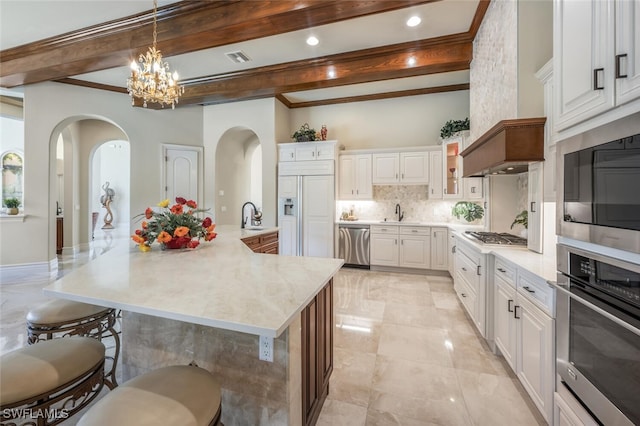 kitchen featuring beamed ceiling, arched walkways, decorative backsplash, built in appliances, and a kitchen breakfast bar