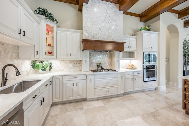 kitchen featuring beam ceiling, a sink, stainless steel appliances, arched walkways, and light countertops