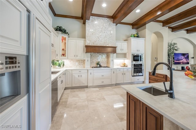 kitchen featuring beamed ceiling, a sink, tasteful backsplash, white cabinetry, and appliances with stainless steel finishes