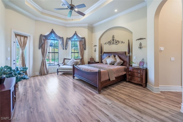 bedroom with arched walkways, light wood-style flooring, a raised ceiling, and ornamental molding