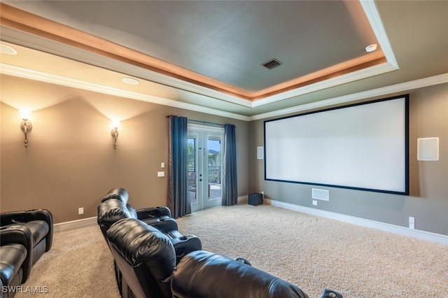 home theater room featuring a tray ceiling, carpet, visible vents, and ornamental molding