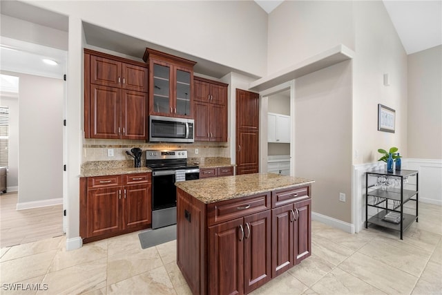 kitchen with light wood-type flooring, backsplash, high vaulted ceiling, appliances with stainless steel finishes, and light stone countertops