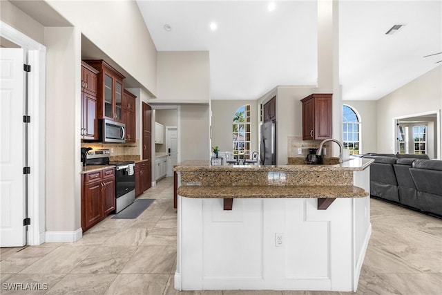 kitchen featuring stainless steel appliances, decorative backsplash, kitchen peninsula, light tile patterned floors, and a kitchen breakfast bar