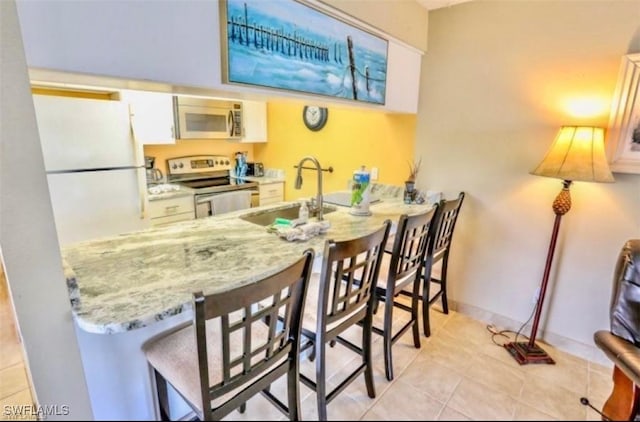 kitchen with appliances with stainless steel finishes, white cabinetry, sink, light stone countertops, and light tile patterned floors