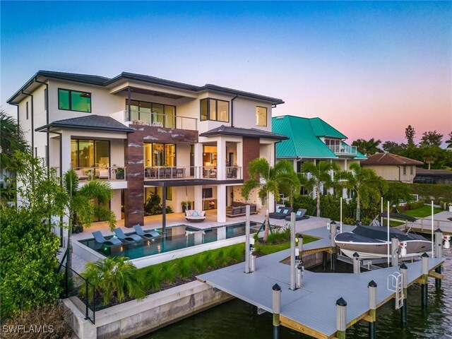 back house at dusk featuring a patio, a water view, and a balcony