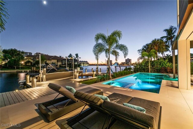 pool at dusk with a dock, a water view, and a patio area