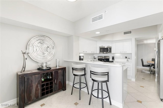 kitchen with white cabinets, a kitchen breakfast bar, light tile patterned floors, appliances with stainless steel finishes, and kitchen peninsula