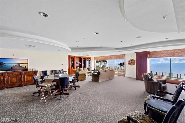 dining room with light carpet, a water view, and a raised ceiling