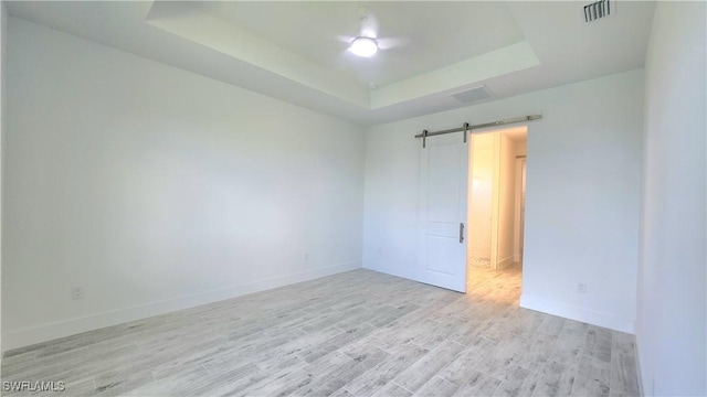 empty room with a tray ceiling, a barn door, and light hardwood / wood-style flooring