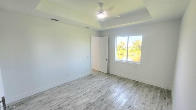 empty room with ceiling fan, a raised ceiling, and light hardwood / wood-style flooring