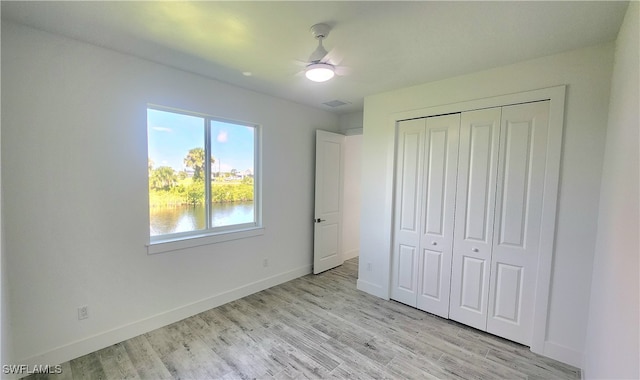 unfurnished bedroom featuring a closet, light hardwood / wood-style floors, ceiling fan, and a water view