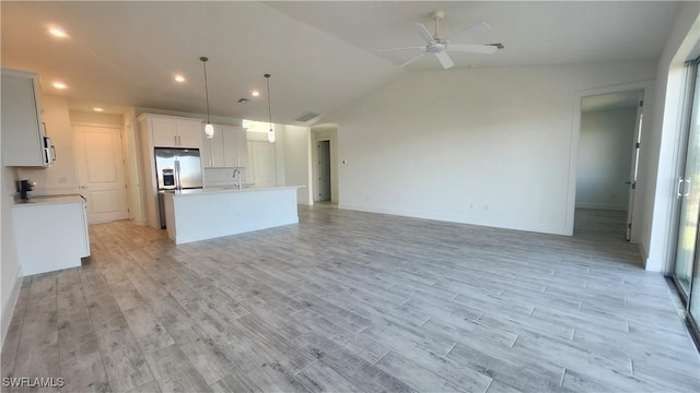 kitchen featuring lofted ceiling, light wood-type flooring, an island with sink, decorative light fixtures, and white cabinetry