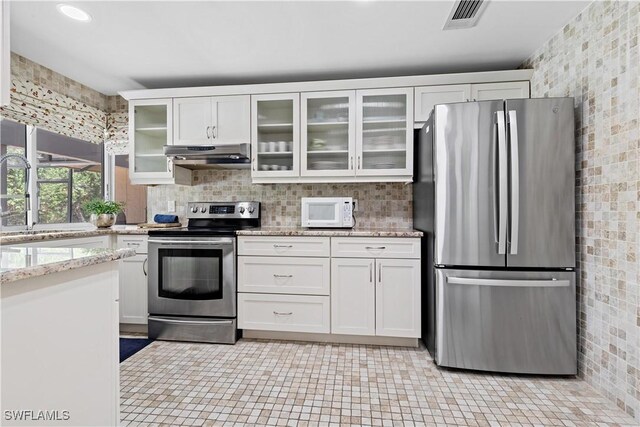 kitchen with white cabinetry, light tile patterned floors, stainless steel appliances, and light stone countertops