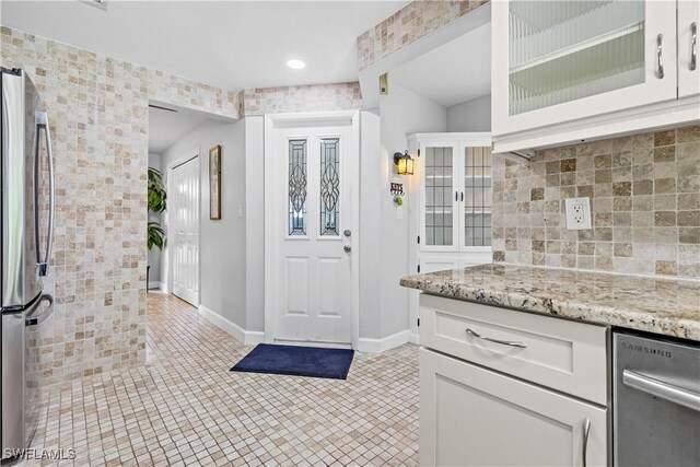 kitchen with tasteful backsplash, stainless steel refrigerator, light stone countertops, white cabinets, and light tile patterned flooring