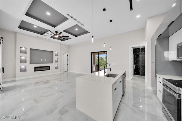 kitchen with coffered ceiling, a kitchen island with sink, appliances with stainless steel finishes, ceiling fan, and decorative light fixtures