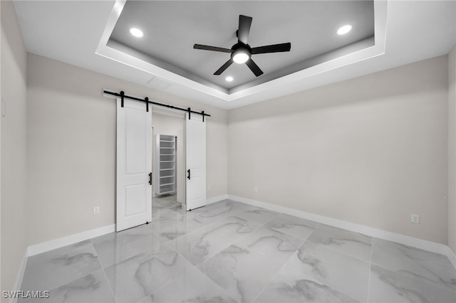 unfurnished bedroom featuring a raised ceiling, light tile patterned floors, a closet, ceiling fan, and a barn door