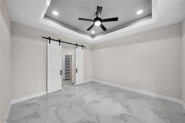 empty room with marble finish floor, a tray ceiling, a barn door, and baseboards