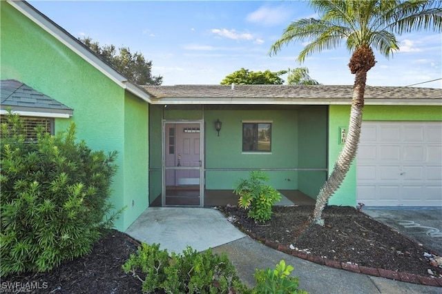 entrance to property with stucco siding, a garage, and roof with shingles