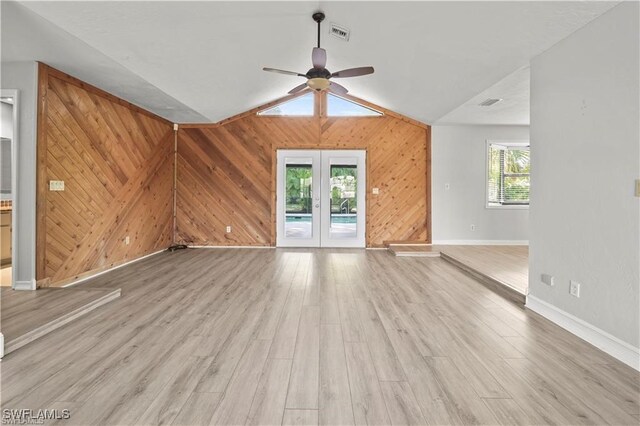 unfurnished living room with wood walls, light hardwood / wood-style flooring, a healthy amount of sunlight, and lofted ceiling