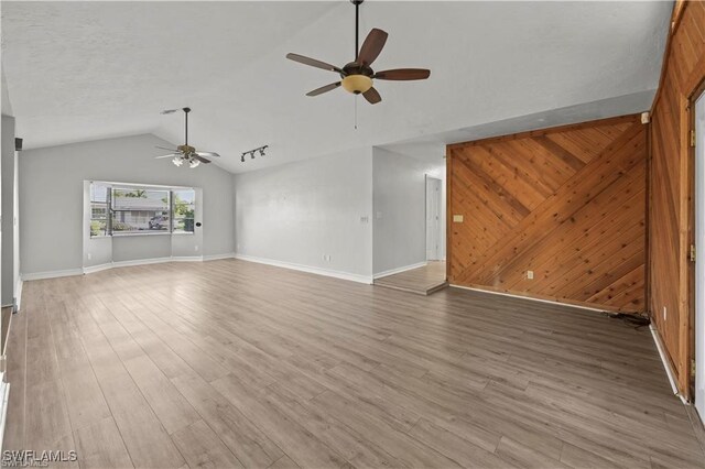 unfurnished living room with hardwood / wood-style flooring, wood walls, lofted ceiling, and ceiling fan