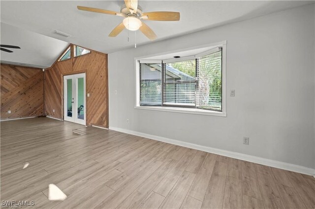 unfurnished room with ceiling fan, light hardwood / wood-style floors, wooden walls, and lofted ceiling