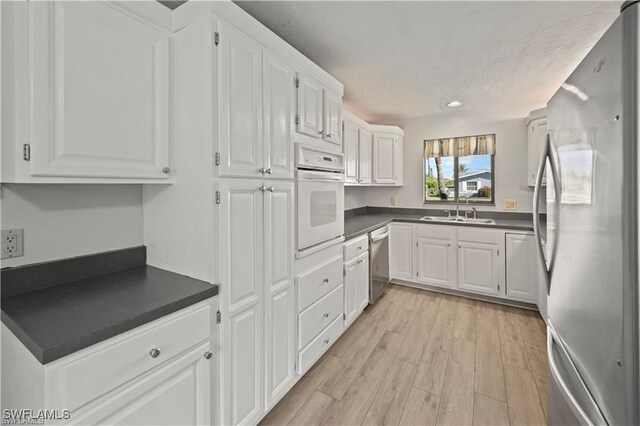 kitchen with light hardwood / wood-style floors, appliances with stainless steel finishes, sink, and white cabinets