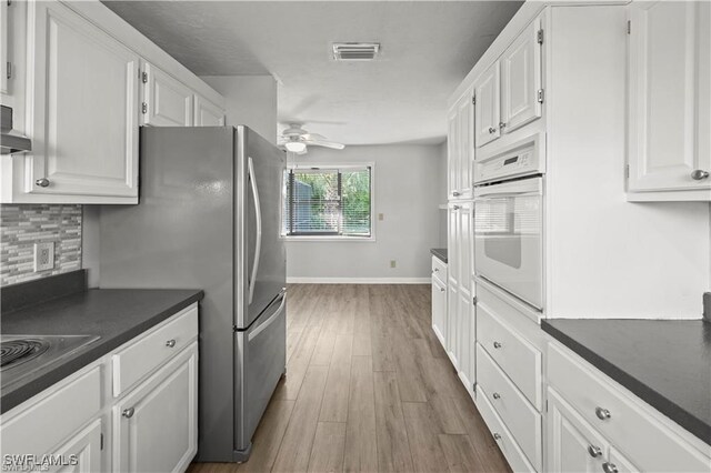 kitchen with white cabinets, white oven, light hardwood / wood-style floors, and ceiling fan