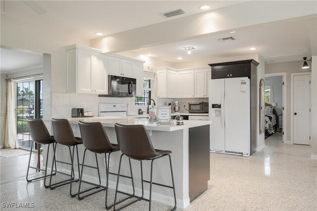 kitchen with stove, a breakfast bar, white refrigerator with ice dispenser, white cabinetry, and an island with sink