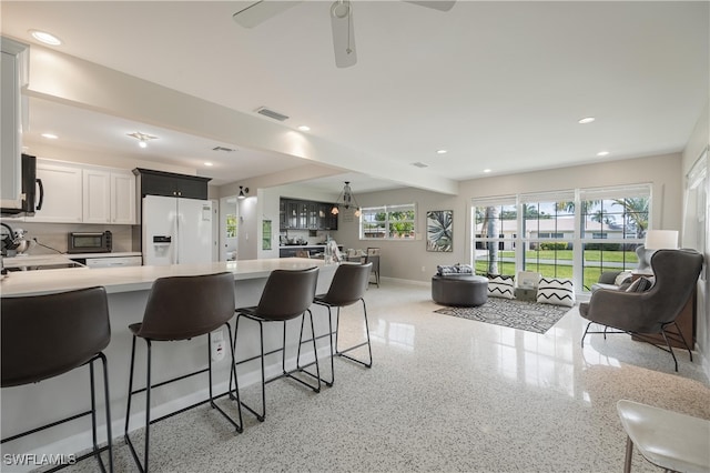 kitchen featuring ceiling fan, white fridge with ice dispenser, kitchen peninsula, a kitchen bar, and white cabinets